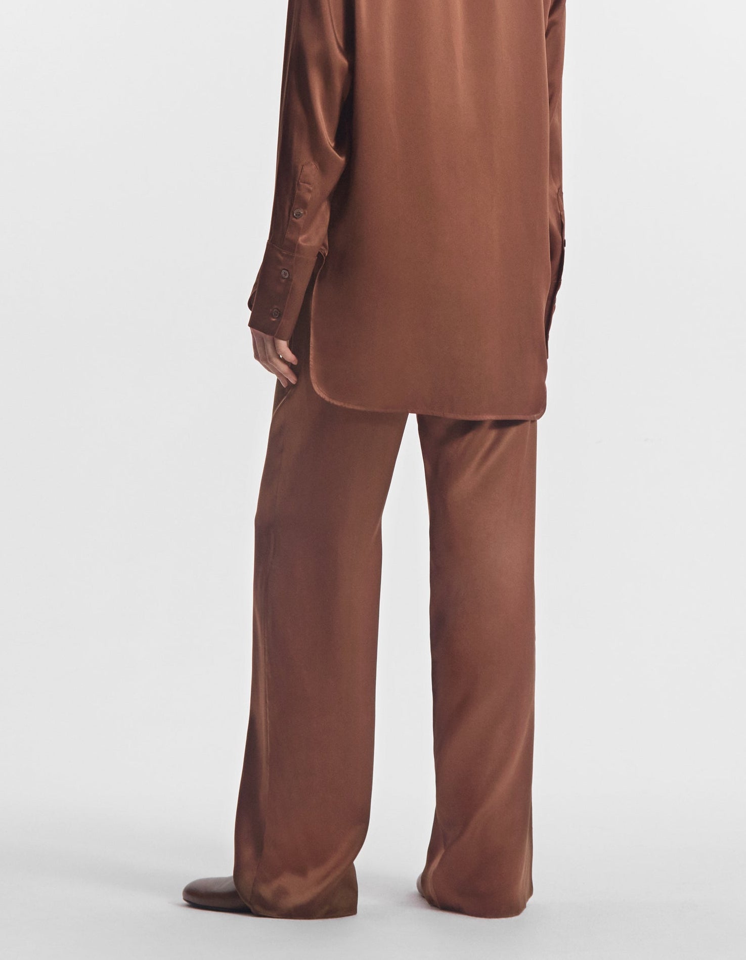 A person wearing a brown silk satin long-sleeve shirt and CO Elastic Silk Pant by CO, viewed from the back against a plain white background.
