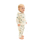 A toddler stands barefoot in the Angel Dear French Terry Zip Hoodie and Jogger Set, featuring a cream tone and playful dinosaur print, looking off to the side against a plain white background.