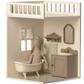 A Maileg stuffed rabbit is in the House of Miniature Bathroom by Maileg, with sink, mirror, towel, and lace curtain furniture pieces on a white and beige background.