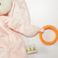 Close-up of Blossom's Activity Toy by Bunnies By the Bay: a soft bunny toy with pink polka-dot and striped fabric, featuring a yellow-orange teething ring and a label with carrot illustrations to boost sensory development.