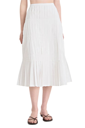 A person wearing the Litus Skirt by Merlette New York, a white pleated midi skirt, paired with black strappy flat sandals.