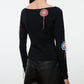 A woman wearing the Staud Rimini Top—a slim, long-sleeve style featuring a boat neckline and vibrant circular crochet appliqué patches on the back and sleeves—paired with black leather pants.