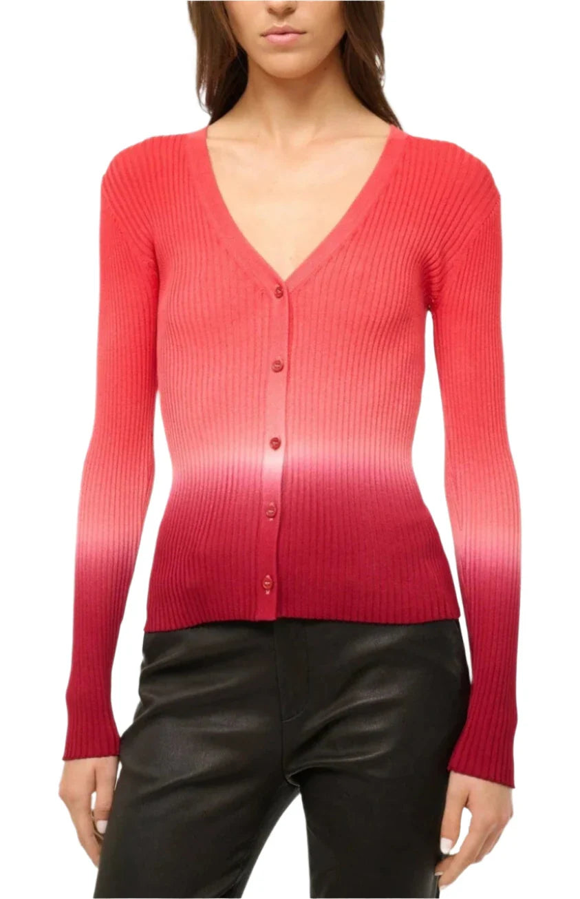 A person wearing the Staud Cargo Sweater, a ribbed cardigan featuring a red to pink dip-dye print, paired with black pants.