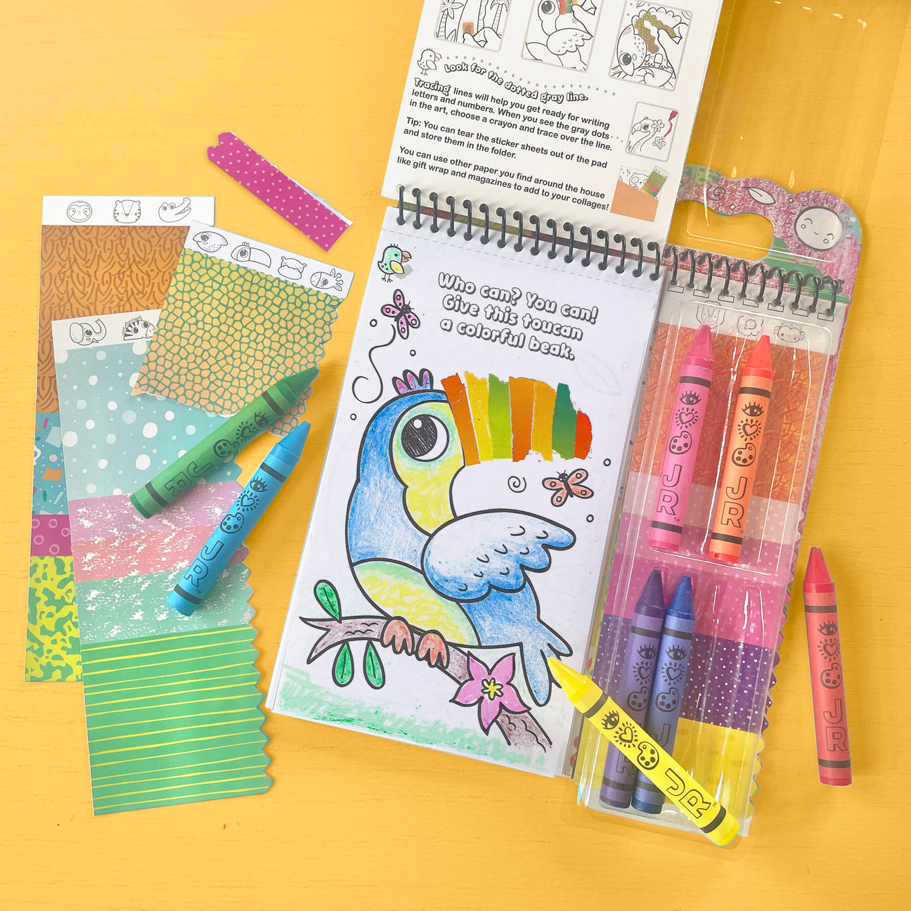 Bright Stripes’ Art on the Go! features a bird coloring book page partially colored with crayons, surrounded by crayons, patterned paper sheets, and sticker tape on a yellow surface—perfect for vibrant creative activities.