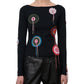 A woman wearing the Staud Rimini Top—a black, slim-fitting long-sleeve shirt with multicolored crocheted doily appliqué and a subtle boat neckline—paired with black leather pants.