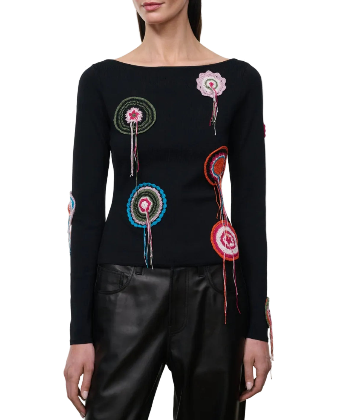 A woman wearing the Staud Rimini Top—a black, slim-fitting long-sleeve shirt with multicolored crocheted doily appliqué and a subtle boat neckline—paired with black leather pants.