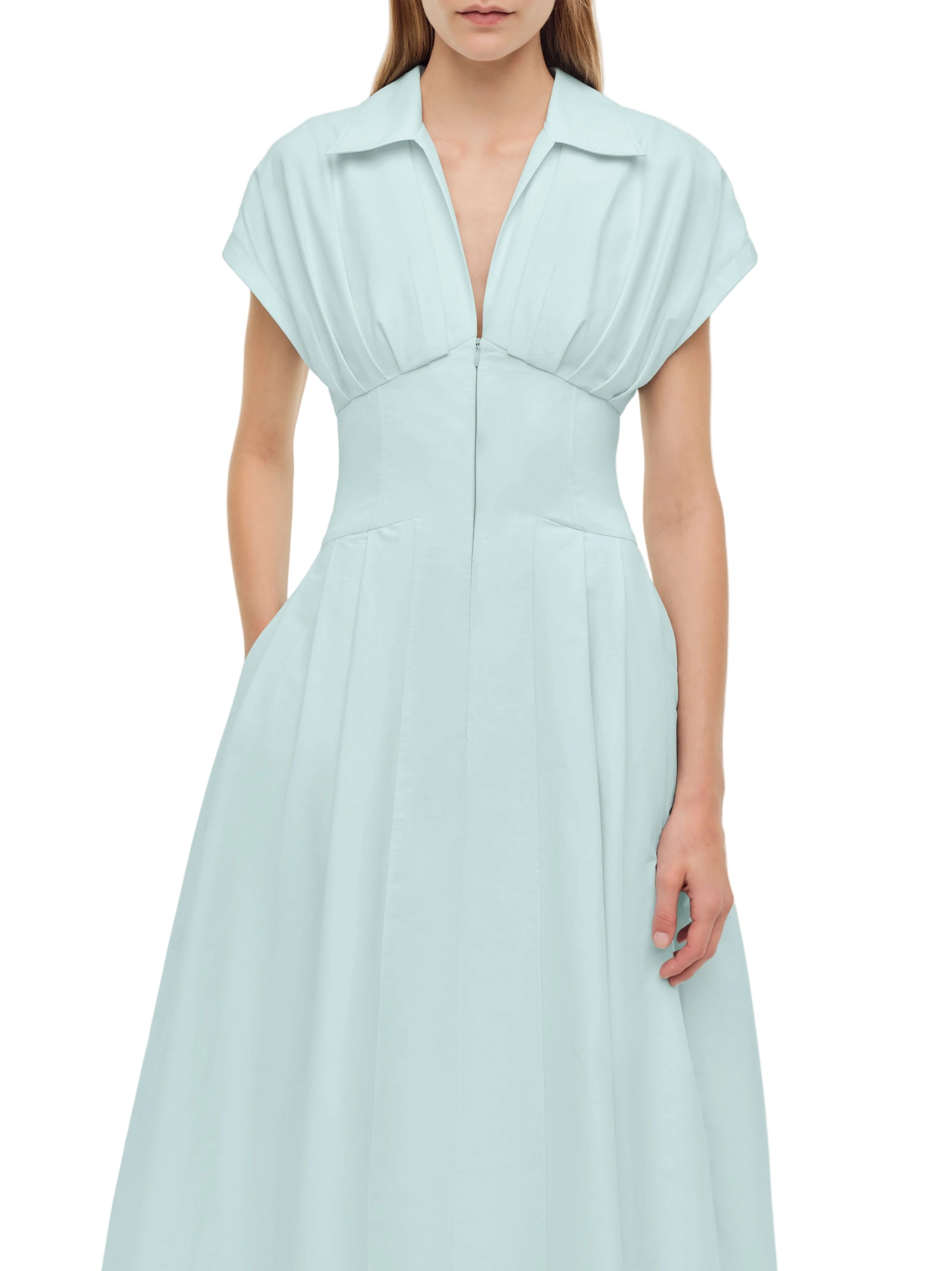 A woman wears the Simkhai Farlow Dress—a polished, light blue cotton faille midi with short sleeves, pleats, and a front zipper.