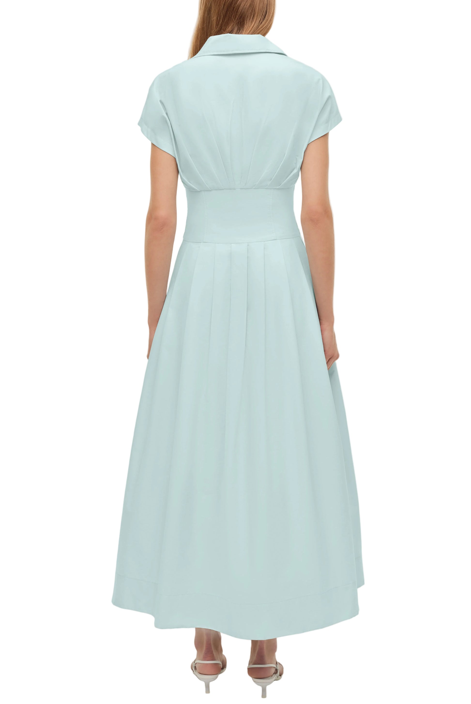 A woman models the Simkhai Farlow Dress, a light blue cotton faille midi with short sleeves and a fitted waist, offering a polished, understated look from the back.
