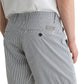 A person wears the AG Jeans Cipher Short in blue and white pinstripe seersucker, featuring a mid-rise waist, belt loops, pockets, and a metallic logo label above the right pocket, paired with a white shirt.