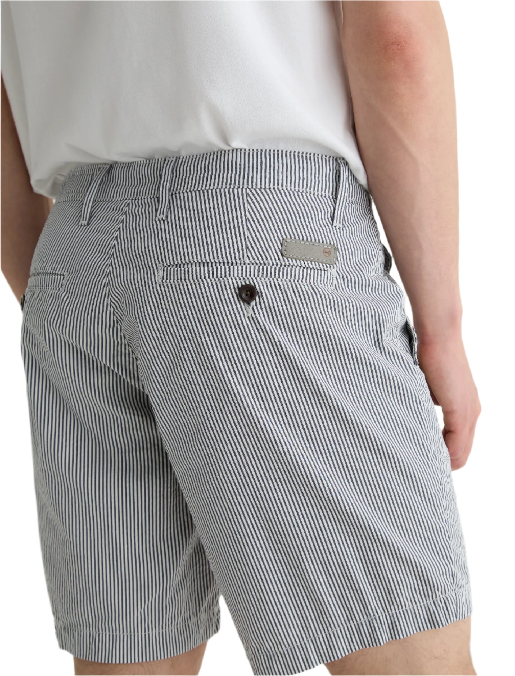 A person wears the AG Jeans Cipher Short in blue and white pinstripe seersucker, featuring a mid-rise waist, belt loops, pockets, and a metallic logo label above the right pocket, paired with a white shirt.