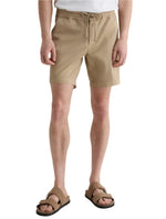 Someone wears AG Jeans' Oliver Short, a high-rise design in breathable twill with an adjustable drawstring, paired with brown sandals, standing against a plain white background.
