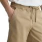 A person wearing a white t-shirt and AG Jeans Oliver Short in tan, featuring a breathable twill blend and adjustable drawstring waist, with hands in pockets.
