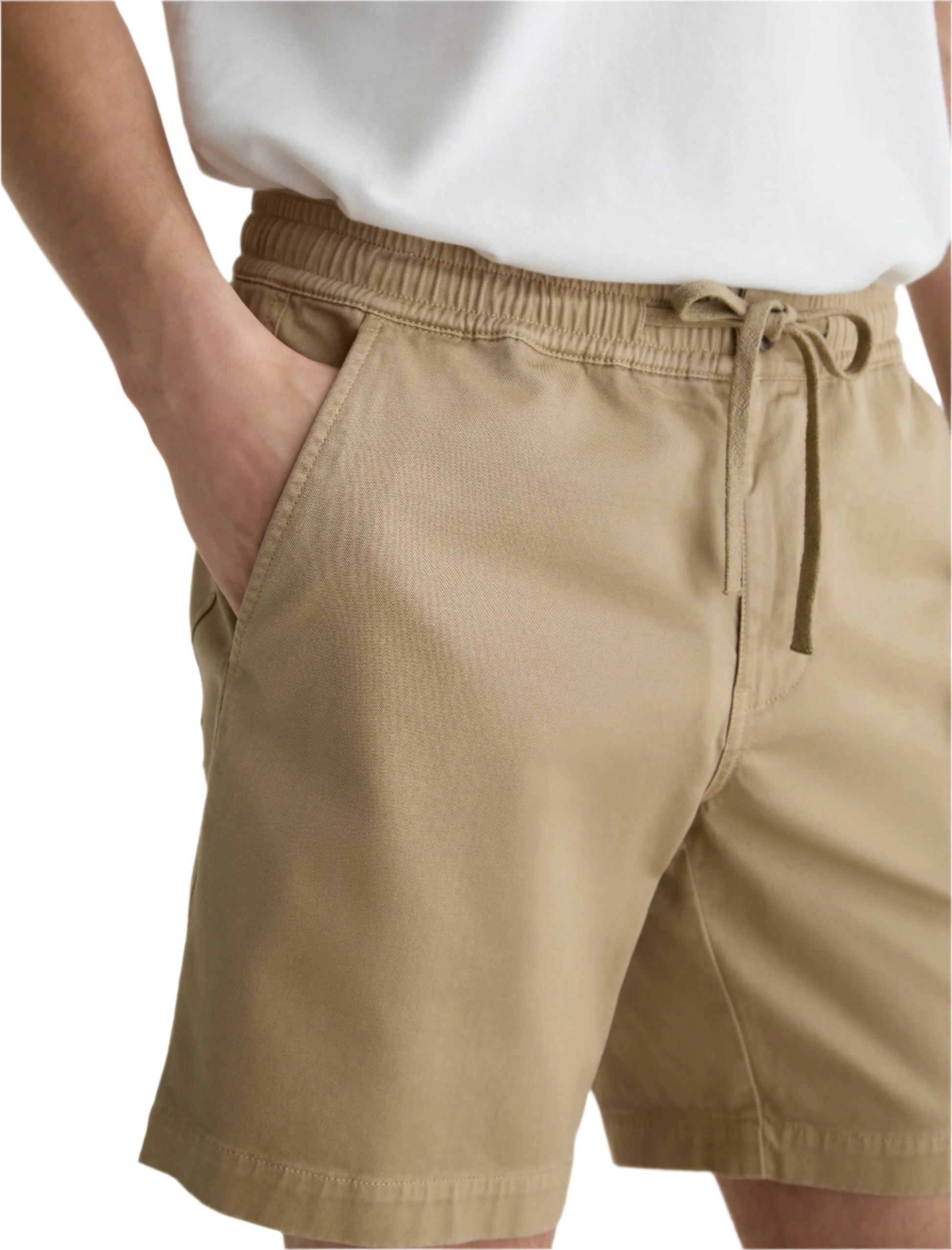 A person wearing a white t-shirt and AG Jeans Oliver Short in tan, featuring a breathable twill blend and adjustable drawstring waist, with hands in pockets.