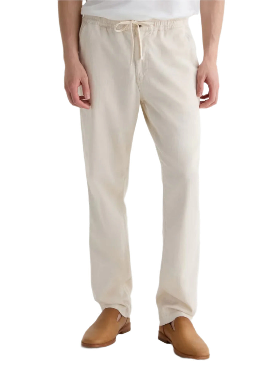 A person is shown from the waist down wearing AG Jeans' Tate Drawstring Pant in relaxed soft twill linen with tan shoes, standing against a plain background.