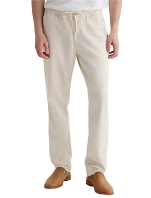 A person is shown from the waist down wearing AG Jeans' Tate Drawstring Pant in relaxed soft twill linen with tan shoes, standing against a plain background.