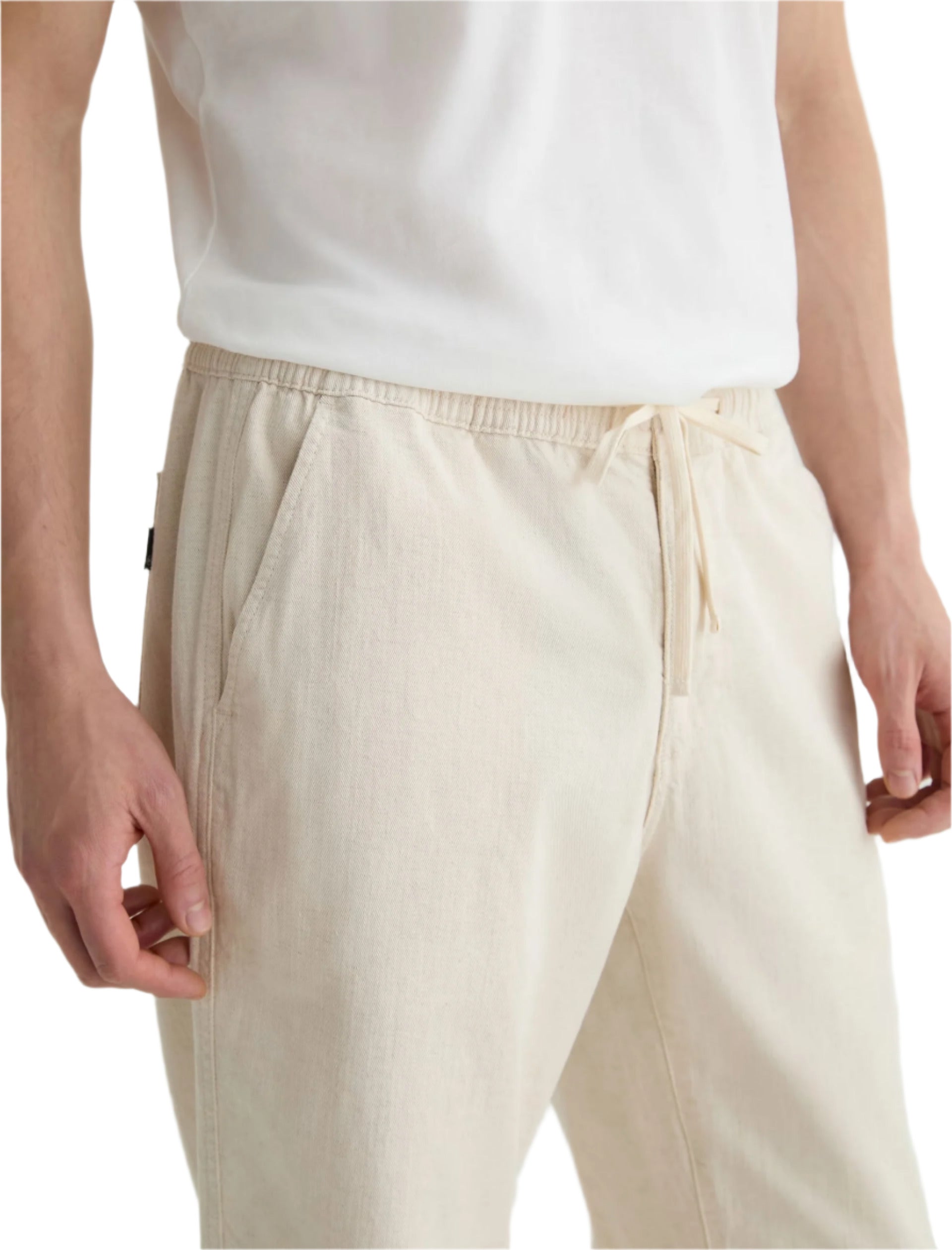 A person wearing a white T-shirt and AG Jeans Tate Drawstring Pant in khaki stands with hands relaxed at their sides.