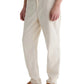 A person wears AG Jeans' Tate Drawstring Pant in light beige, paired with a white shirt and tan slip-on shoes, shown from the waist down against a white background.