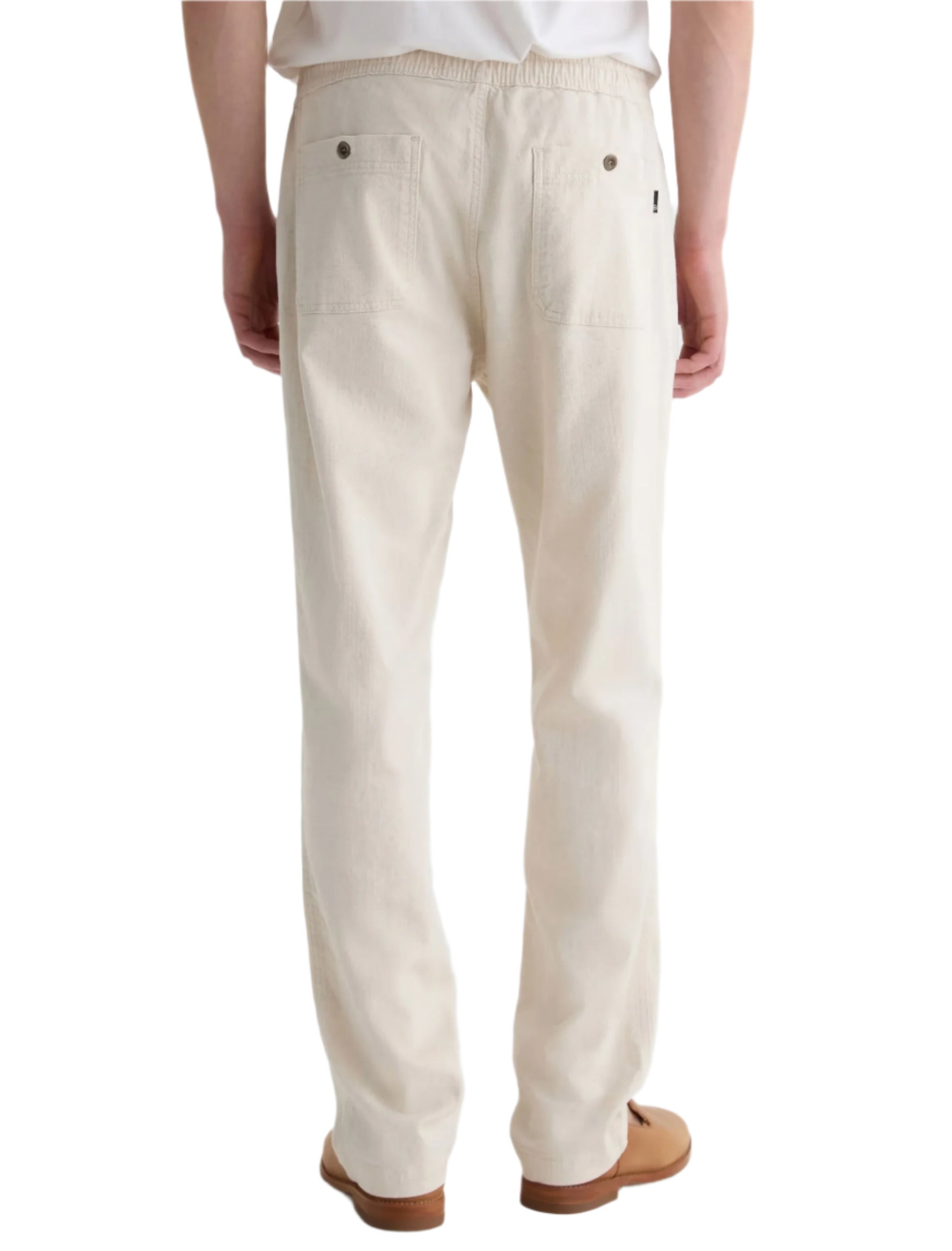 A person wearing AG Jeans' Tate Drawstring Pant in off-white twill linen, paired with a white shirt and brown shoes, viewed from the back.