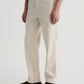 Wearing the Archie Sueded Trouser by AG Jeans in a cream shade with a relaxed straight-leg fit, paired with brown suede shoes, the individual stands against a plain light background.