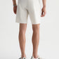 An athletic model is shown from the back wearing a gray sweater, AG Jeans Bay Short in a modern off-white summer silhouette that reaches the knees, and white sneakers with black accents.