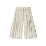 CO’s Pleated Culotte features wide legs, front pleats, a matching fabric belt, and comes in light beige, shown against a white background.