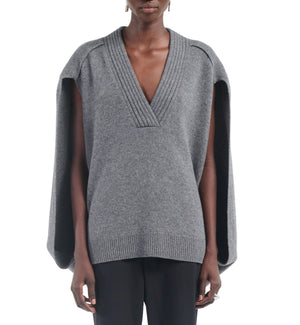 A person wears the gray Maria McManus Cocoon Cape, an alpaca-wool blend with a deep V-neck and wide cape-like sleeves, styled with black pants.