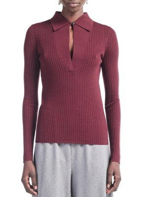 A person wears the Maria McManus Single Button Polo—a slim-fit, ribbed long-sleeve burgundy knit with a collar and keyhole detail—paired with light gray pants.