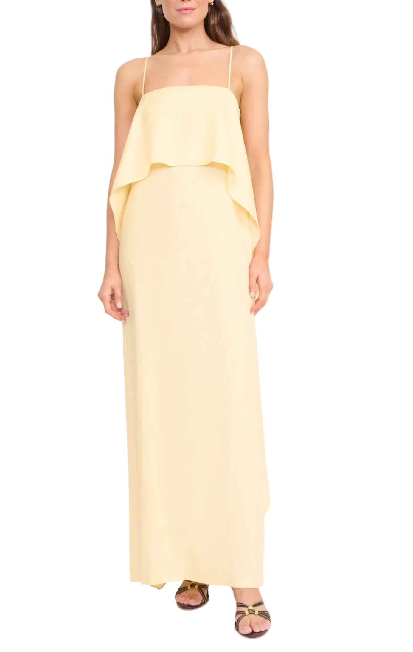 A woman wears the Staud Valencia Linen Dress—a sleeveless, light yellow dress with adjustable straps and layered ruffle bodice detail—paired with flat sandals.