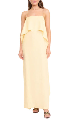 A woman wears the Staud Valencia Linen Dress—a sleeveless, light yellow dress with adjustable straps and layered ruffle bodice detail—paired with flat sandals.