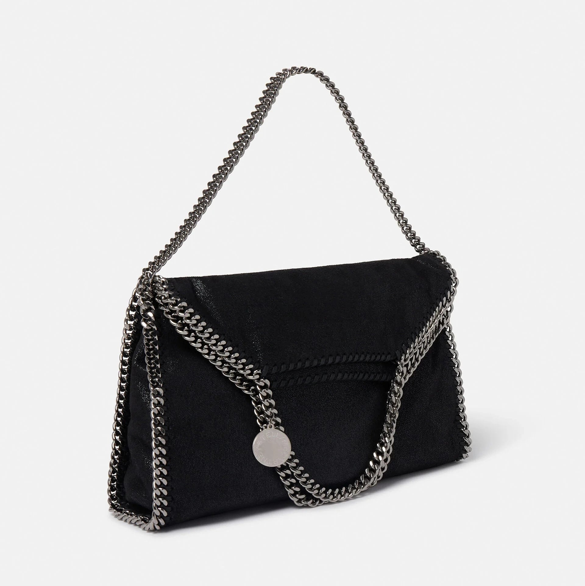 The Falabella Fold Over Tote by Stella McCartney is a black envelope-style vegan bag with chain edges and strap, plus a round metallic charm. Crafted from recycled plastic bottles, it's inspired by the iconic Falabella tote.
