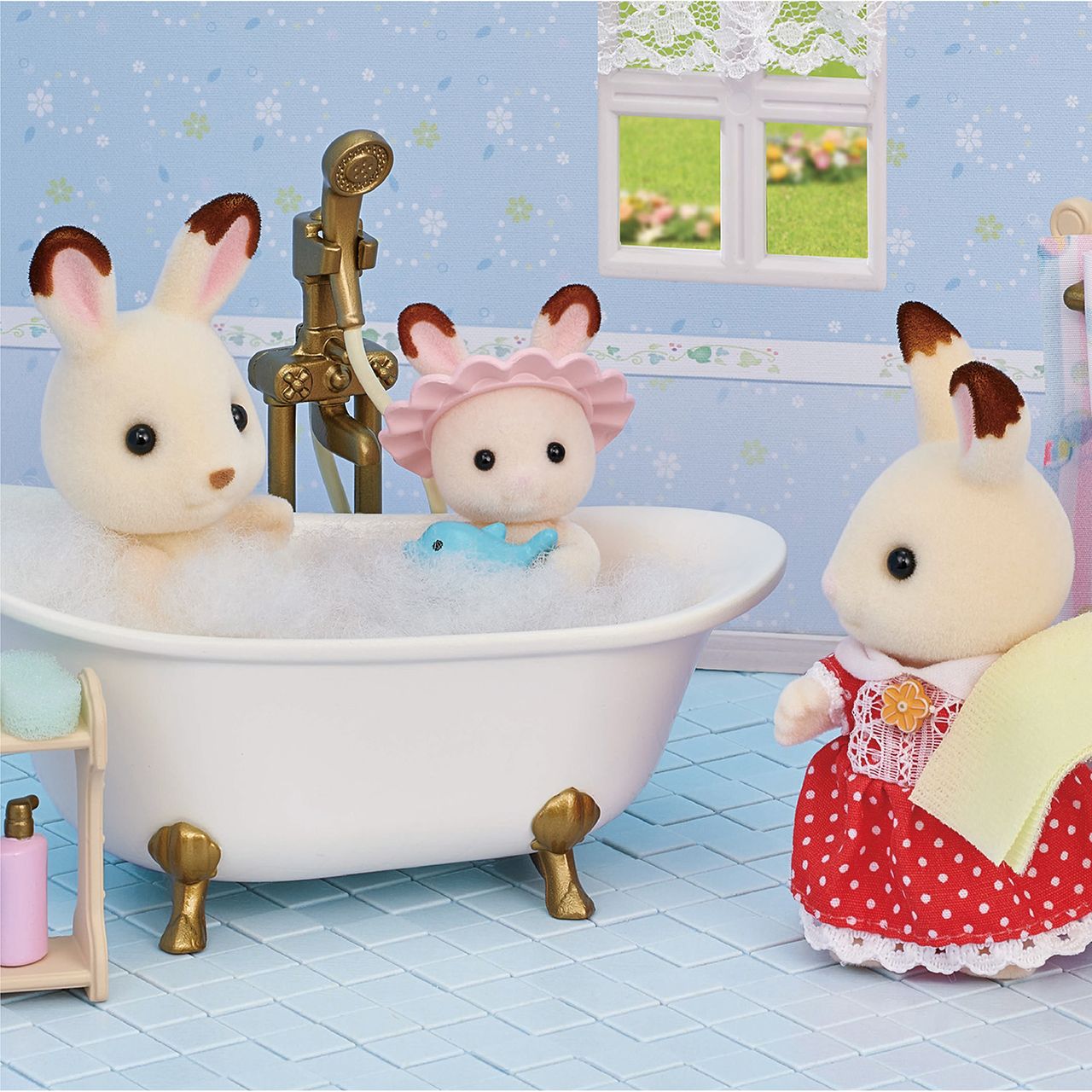 Three Calico Critters from the Bath & Shower Set are in a bathroom scene: one enjoys a bubble-filled bathtub with a toy fish and bath time accessories, another stands nearby dressed in red, and the third sits beside an antique-style bath fitting.