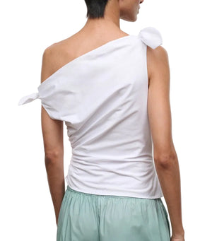 A person is shown from the back against a white background, wearing the Staud Bellaria Top—a white one-shoulder evening top with tied details and an asymmetrical neckline—paired with light green shorts.