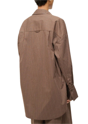 A person is seen from the back wearing the Staud Sandbar Top, a boxy button-up shirt in brown and white stripes from Staud, perfect as a stylish swim cover-up.