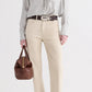 A person dressed in a striped shirt, beige pants, dark belt, and sandals holds the Small Howard Bag by TWP in Cognac leather, lending a refined touch and structured silhouette to the ensemble.