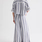 A person stands with their back to the camera, wearing a loose-fitting blue and white vertical stripe shirt paired with TWP's Demie Linen Stripe Pant.