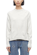 Woman in a 3.1 Phillip Lim Merino Knit Top with an asymmetric hemline and blue jeans standing against a white background.