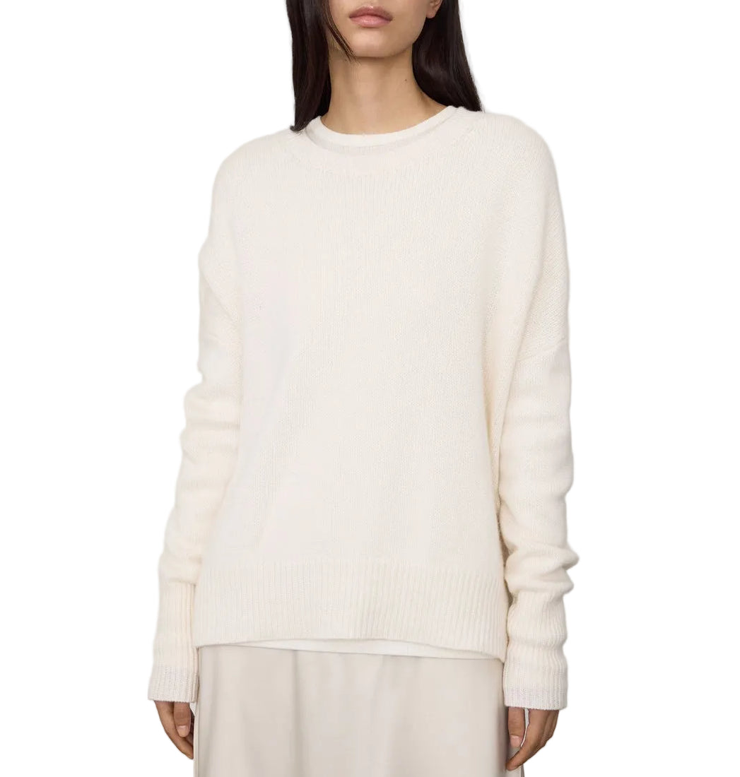 A woman stands against a plain white background wearing the Lisa Yang Mila Cashmere Sweater in off-white with a light-colored skirt.