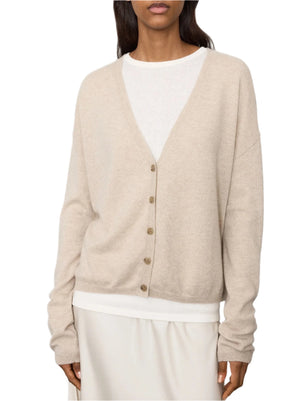 A person is elegantly dressed in the Lisa Yang Lisa Yand Abby Cashmere Cardigan in beige, layered gracefully over a crisp white shirt.
