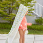 A young child outdoors wears a sun-patterned swimsuit and drapes the Timo & Violet Hooded Bath Towel, featuring playful prints, over their head and shoulders like a cape.