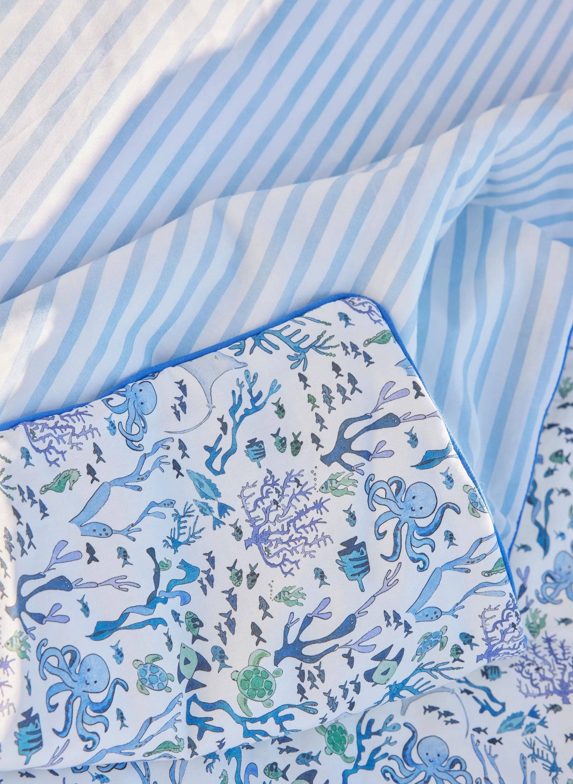 Close-up of Timo & Violet Crib Quilt bedsheets—one in blue and white stripes, the other featuring ocean-themed illustrations with octopuses, fish, and coral.