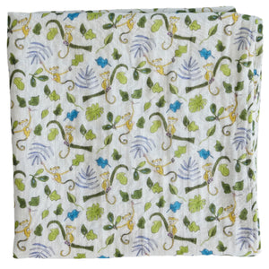 The Timo & Violet Shawl Blanket is a folded white organic cotton baby accessory with a playful print of monkeys, green leaves, and branches in shades of green, brown, and purple—ideal for adding style to any nursery.