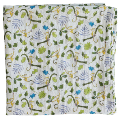 The Timo & Violet Shawl Blanket is a folded white organic cotton baby accessory with a playful print of monkeys, green leaves, and branches in shades of green, brown, and purple—ideal for adding style to any nursery.