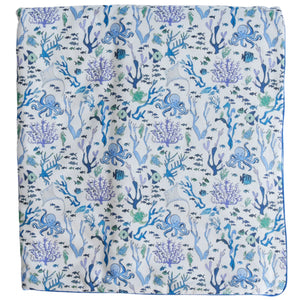 The Timo & Violet Crib Quilt is a square cloth with octopuses, fish, coral, and seaweed in blue, green, and purple on white—an eco-friendly bedding choice for your nursery.