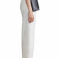 Person standing in profile view, wearing a white knit top, Apiece Apart Classic Merida Pant by Apiece Apart, black loafers, and a small black crossbody bag.