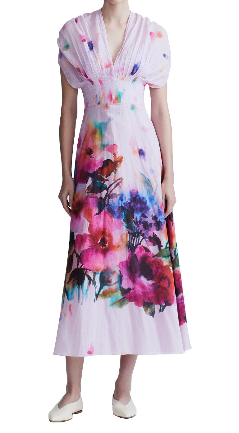 Person wearing a Lela Rose Watercolor Floral Cotton Voile Isabel Dress by Lela Rose made from airy cotton voile with short sleeves and a deep V-neck, paired with white shoes. The dress features a whimsical watercolor floral print.