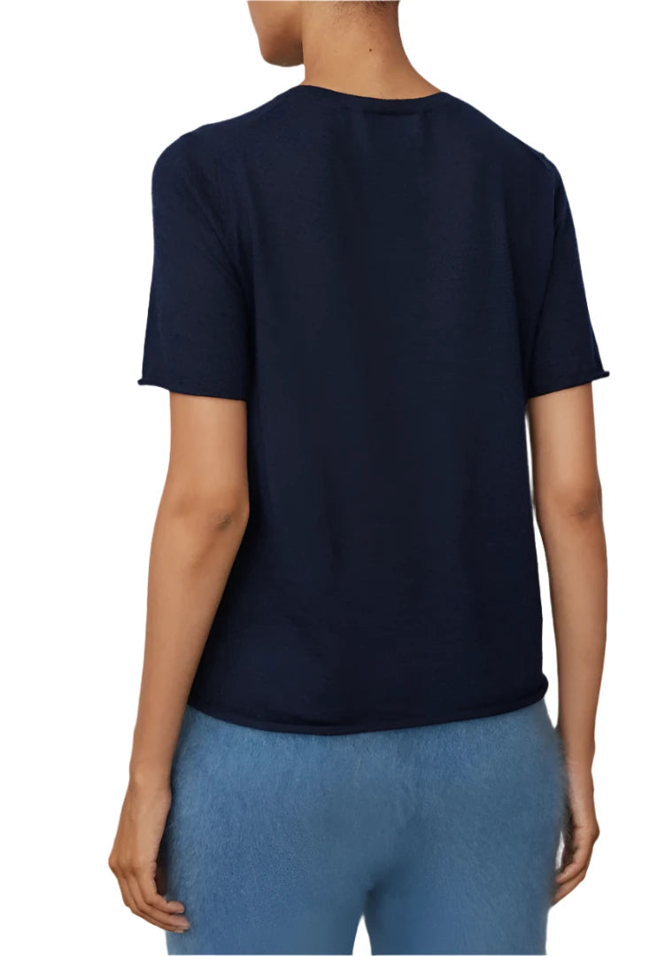 A person is shown from the back wearing a Lisa Yang Ari Cashmere T-Shirt in dark blue, paired with light blue pants.