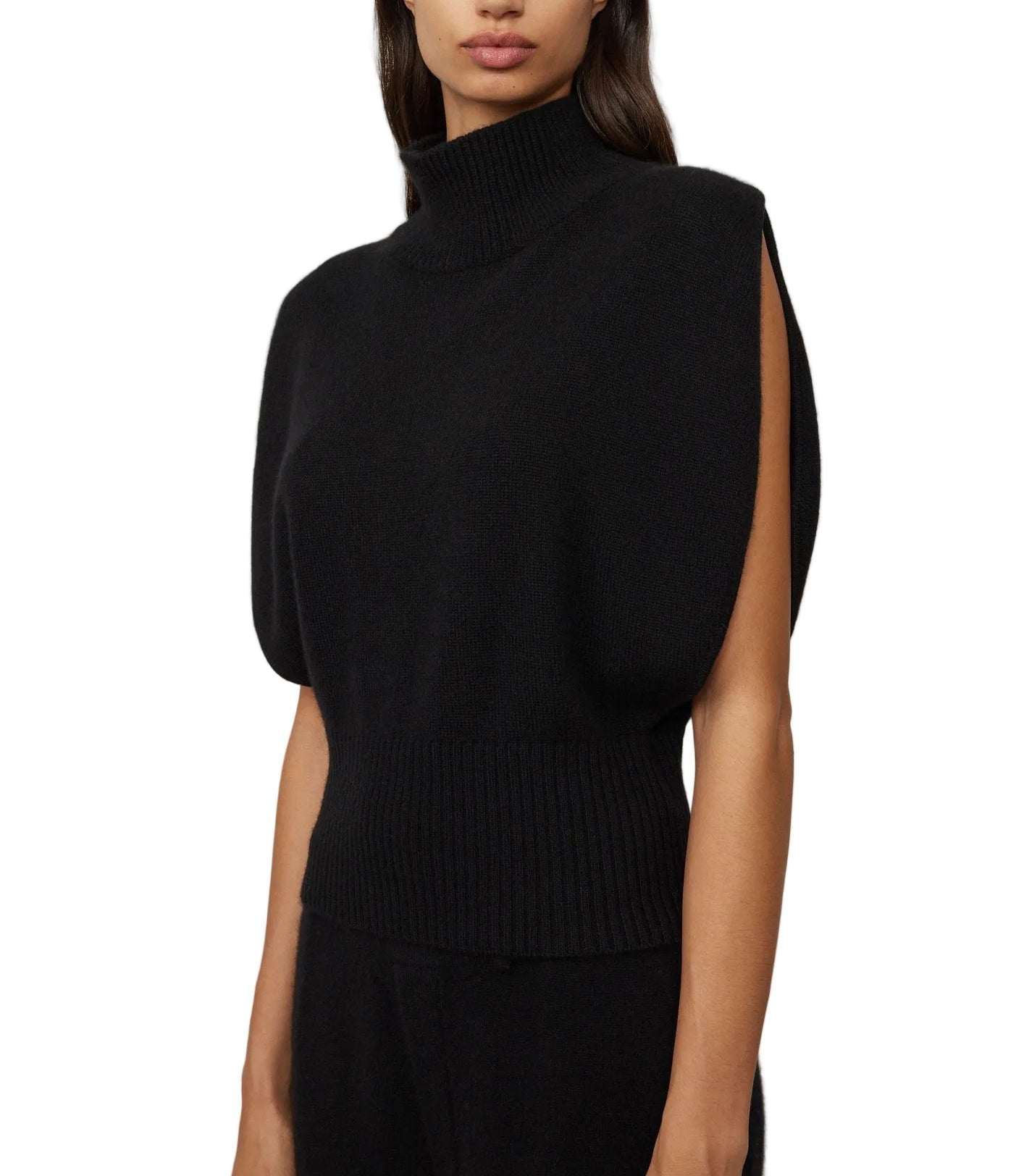 A woman wears the Zaya Top by Lisa Yang, a sleeveless black cashmere top featuring a high neck, wide arm openings, and ribbed detailing at the waist and neck.