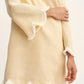 Wearing the Essie Kaftan by POSSE, this style features a light yellow linen fabric, long sleeves, deep v-neckline, and scalloped hems with white fringe trim—ideal for a chic vacation dress look.