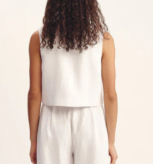 A person with curly hair is shown from behind, wearing POSSE's Rio Top—a sleeveless white high-neck top—paired with matching relaxed-fit linen pants, set against a plain background.
