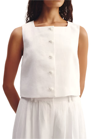 A woman wearing the POSSE Rio Top—a sleeveless white, relaxed-fit top with a square neckline and front buttons—paired with white pleated pants.